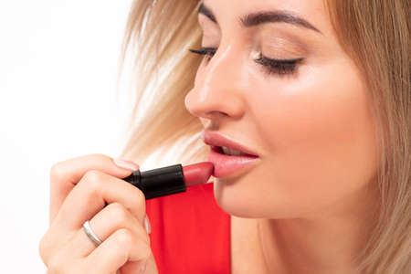 The girl paints her lips. Close-up of a woman's face painting her lips. Makeup. Female beauty. A beautiful blonde puts on lipstick. Natural make up.の写真素材