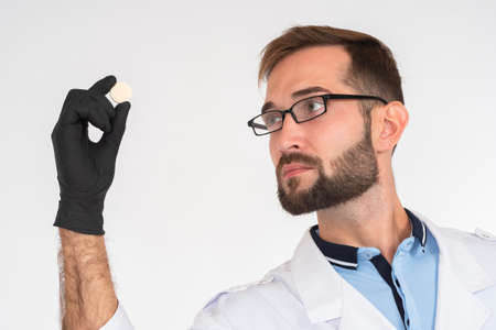 Male doctor holds a pill in his hand. Hospital medical examiner shows the pill to take to his patient. Advertising of medicines. Use of medications as prescribed by a doctor.の写真素材