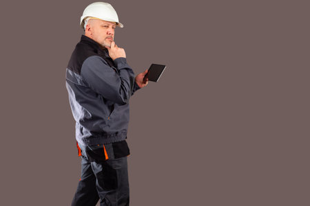 Thoughtful worker with a tablet in his hands. A man in a work uniform studies the details of the...