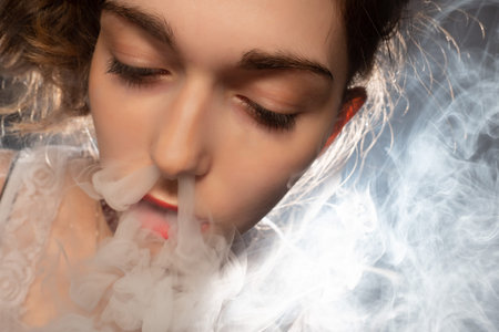 Close-up of a female vaper face. A girl in a cloud of smoke from an electronic cigarette. A woman...