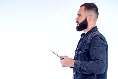 Guy with a gadget on a light background. A bearded man holds a smartphone in his hands and looks...