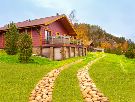 Two-story wooden house. A stone path leads to the house. Cottage on the background of autumn nature....