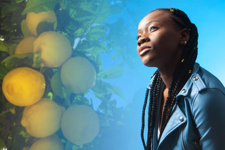 Dark-skinned girl with braids on the background of a lemon tree. An African-American woman remembers her Homeland. Dark-skinned model on a bright natural background. The dream of travel.の写真素材