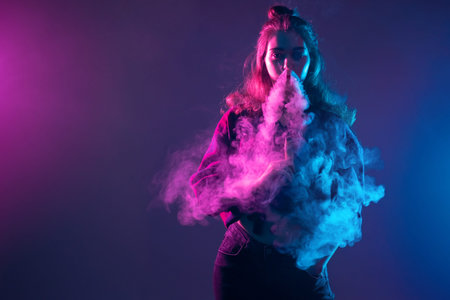 The girl lets out smoke from the VAPE in the neon light. A young long-haired girl smokes an...
