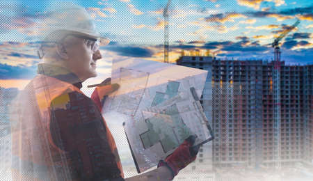 Construction. Engineer in a white helmet on the background of buildings under construction. Builder on the background of the contours of cranes and frames of a building under construction.の写真素材