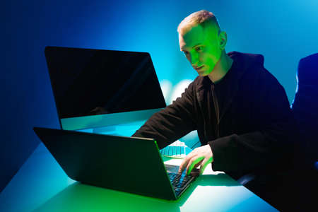 Computer addiction. A man works at a computer. The face of the person behind the laptop is illuminated in green light. Excessive fascination with gadgets.の写真素材