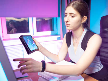 The work of a stock analyst. The girl conducts an analysis of stock prices. A woman with documents and a tablet at her Desk. Analysis of exchange information.の写真素材