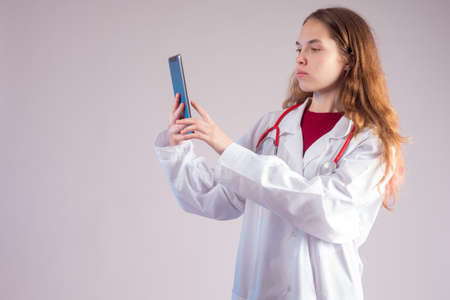 Telemedicine. Remote medical consultations. Girl doctor with a smartphone in hand. A doctor in a white coat with a stethoscope around his neck. Student-physician.の写真素材