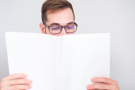 A man with glasses reads paper documents. A man holds business papers, covering part of his face....