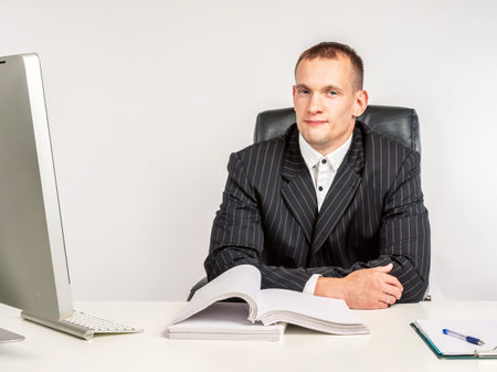 A man at his Desk. A happy man in a business suit. A man sits at a table with documents and looks at the camera. Good job.の写真素材