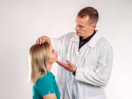 Plastic surgery. The doctor examines the face of a beautiful girl. Cosmetology. Procedures to maintain the beauty. Doctor and patient on a white background.の写真素材