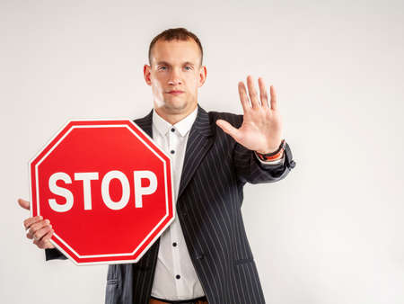 A man with a STOP sign and an outstretched hand. The man gestures and demands to stop. A man with a STOP sign on a white background. A stopping gesture.の写真素材