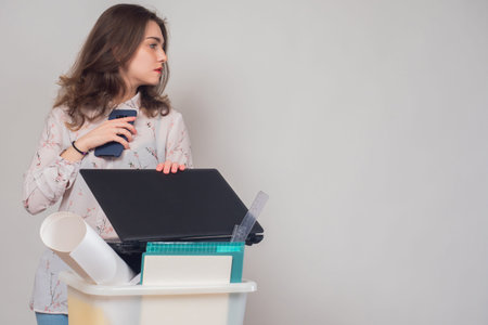 Dismissal from work. A girl with a box of office supplies and a smartphone. Job change. Space for...