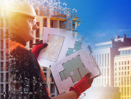 Architect with construction documentation on the background of the building. A man in a white helmet holds construction plans in his hands. Monitoring the progress of construction.の写真素材