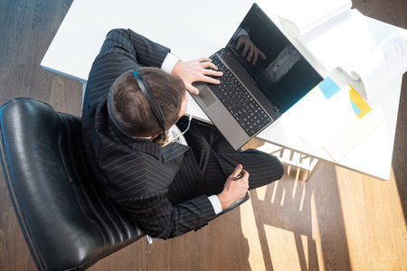 Top view of a man at his Desk. A man in headphones and a business suit is working on a laptop....