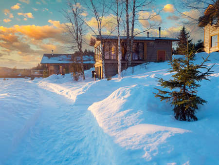 Paths in the snow lead through the cottage village. Private homes against a beautiful sky. Country houses in snowdrifts. View of cottages in winter.の写真素材