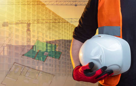 City construction. A Builder with a white helmet in his hands against the background of a building under construction. Project documentation and the house under construction.の写真素材