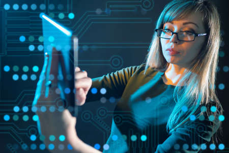 A girl with a tablet in her hands on the background of a printed circuit Board. Computer gadgets. A long-haired woman with glasses searches for information on a tablet.の写真素材