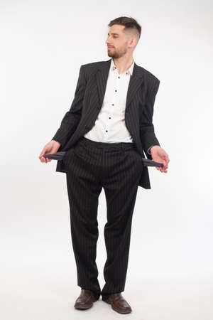 Lack of money. A man in a suit shows empty pockets. A man with empty pockets on a white background. Impoverishment. Loss of savings. Poverty.の写真素材