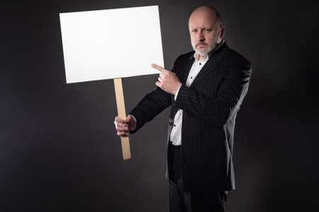 A man in a business suit with a poster. The man points at the poster. Place for text. A frowning...