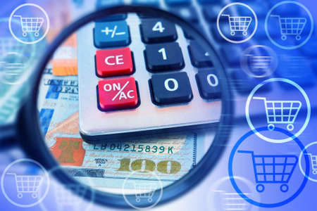 Money for purchases. Consumer basket. Analysis of purchases. Calculator, money and shopping cart on the background of a magnifying glass.の写真素材