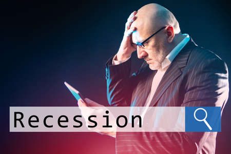 A dumbfounded businessman on the background of a search bar with the word Recession. A man with an electronic tablet clutched his head. Economic problem. Economic crisis.の写真素材