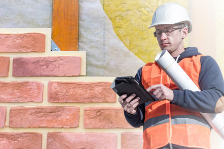 Builder next to the wall of the house. Building materials for walls. A construction worker in a...