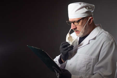 The doctor examines the results of tests. Doctor in rubber gloves with a tablet in his hands. The medical worker has removed the protective mask from his face and is reading the document.の写真素材