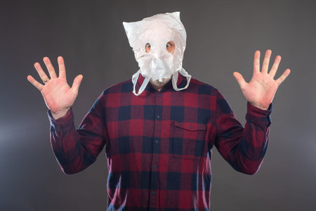 The man put a bag with holes for eyes on his head. The man with the bag on his head spread his...