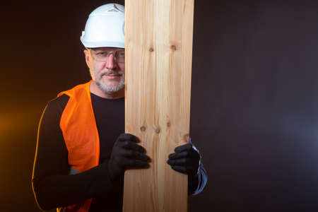 A worker with boards in his hands. The supply of wood. Highly qualified carpenter. Finishing works using wood. Woodworking. Builder in construction vest and helmet with boards in his hands.の写真素材