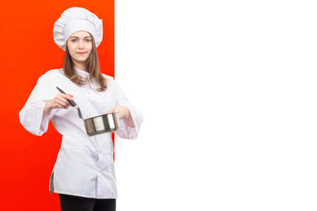 girl in a chef's uniform on a red and white background. Place for text. A woman cook with a ladle in her hand. The girl in the chef's hat. Food preparation. Cooking. Restaurant.の写真素材