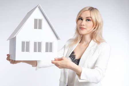 A girl with a model of the house in her hands. Dreams of your own home. Development of construction projects. Blonde with a layout of a cottage. Visualization of a construction project.の写真素材