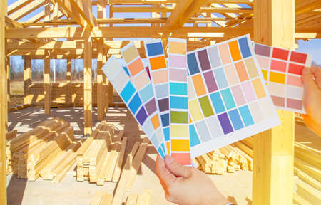 A person holds color palettes in front of a house under construction. Design project of the cottage. Color scheme for the new building. Color selection for interior and exterior finishes.の写真素材