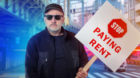 A man with a placard urging not to pay rent, on a city street. Picket. Economic demand. A man in black clothing and glasses draws attention to the difficulties during the quarantine.の写真素材