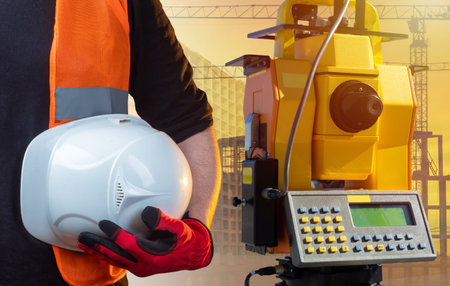 Work of a surveyor in construction. A man in a reflective vest is holding a white helmet. Builder...