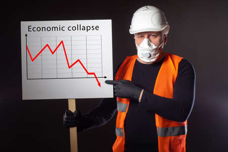 Economic collapse. A man in a mask and rubber gloves points to a poster with a falling economic development schedule. Economic crisis due to coronavirus. Deprivation of means of livelihood. Job loss.の写真素材