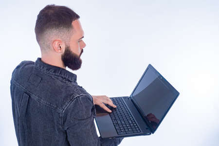 Rear view of a person with a laptop. A man in a denim jacket is holding a laptop. The bearded man works on a portable computer.の写真素材
