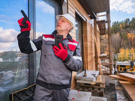 Engineer near the cottage under construction. Construction worker with a smartphone points to a...