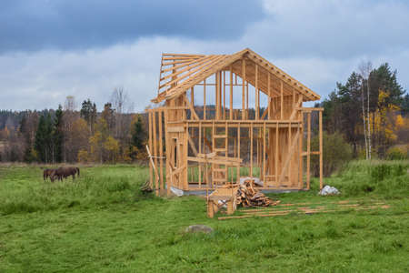Frame of a standing cottage on the background of an autumn landscape. Wooden construction of a house on an open-air construction site. Construction site on the background of nature.の写真素材