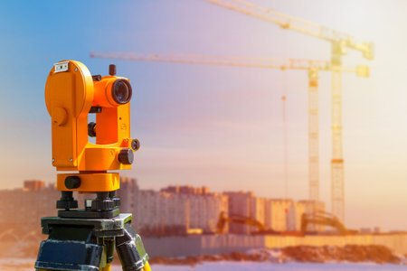 A surveyor works on a construction site. Geodesic equipment is aimed at a house under construction...