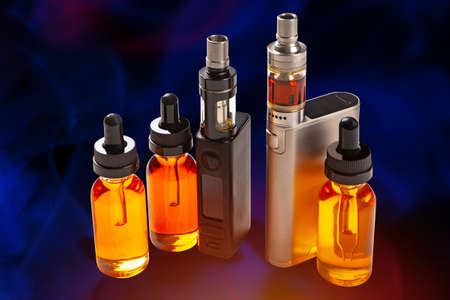 Vapes and vials with liquids close-up. Vaping accessories on a dark background. Gadgets for Smoking. Smoking electronic cigarettes. Electronic cigarettes and liquids on a blue background.の写真素材