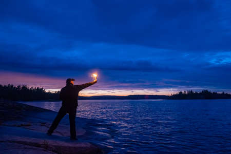 A man gives a signal with a smoke bomb. Smoke signals in the night. A man with a smoke torch by the water. Distress signal. The SOS signal. Call for help. Dangerous situation.の写真素材