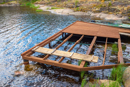 Construction of a boat dock. The future pier for boats and boats on the lake. Wooden flooring at the rocky shore. Infrastructure for water walks.の写真素材
