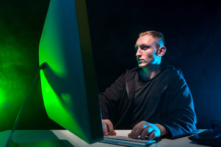 A young man is working at a computer. A man in black clothes looks at the monitor intently. Work in...