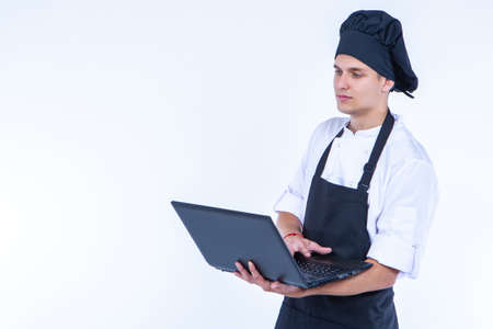 Chef portrait. A man in a chef suit with a laptop in his hands. Electronic cookbook. Cooking recipes. Cook with a laptop in his hands on a white background. Place for text.の写真素材