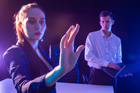 A man and a woman on a dark background with lilac lighting. A man with a laptop looks at a beautiful...