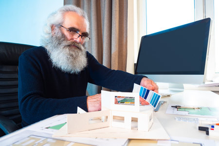 An architect with gray hair and a beard. An elderly man works as an interior designer. The designer...