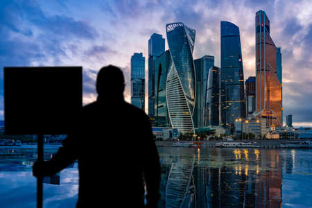 Shadow of a man with a transporter on the background of skyscrapers. Concept - protests due to unemployment. Shadow of a man near Moscow city. Single picket near the business center. Russia.の写真素材