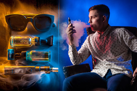 Vaper set. Young guy is vaping. Sunglasses next to vape devices. Man examines an electronic...