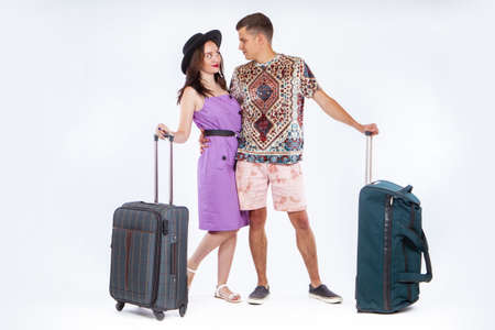Lovers with travel suitcases. Couple of travelers on a white background. Travel suitcases as a symbol of tourism. Young couple travels. Man and a woman. Honeymoon. Travelers in love are huggingの写真素材